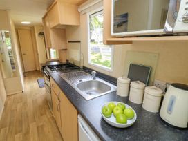 A narrow kitchen with sink stove microwave kettle and containers on the counter at Greenwood in Cowes