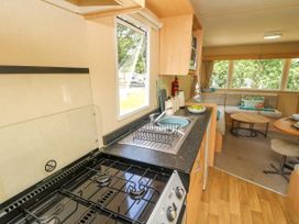 A kitchen area with a gas stove and sink next to a living room with a sofa and coffee table at Greenwood in Cowes