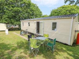 A beige mobile home with open door bicycles parked outside and four folding chairs around a table on grass at Greenwood in Cowes