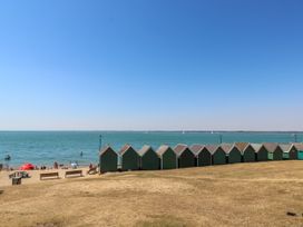 A beach with people umbrellas benches and small green beach huts near the sea at Greenwood in Cowes
