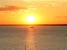 A sunset over a body of water with a boat in the distance and a clear sky at Greenwood in Cowes