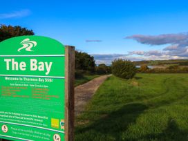 A green information sign for Thorness Bay SSSI next to a dirt path with grass and trees under a blue sky at Greenwood Cowes