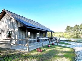 A wooden lodge with decking and flowers near water at Kingfisher Lodge in Treverbyn near St Austell