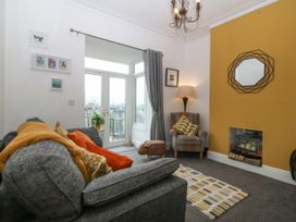 A living room with a grey sofa orange and yellow cushions a yellow accent wall with a fireplace a patterned rug an armchair with cushions a lamp and glass doors leading to a balcony at Terrace View in Trefriw near Llanrwst