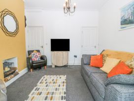 A living room with a gray sofa, orange and yellow cushions, a patterned rug, a black armchair, a wall-mounted TV, and a yellow feature wall with a mirror at Terrace View in Trefriw near Llanrwst