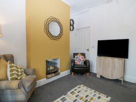 A living room with a plaid armchair a black armchair a flat screen television on a wooden stand a yellow painted fireplace wall and a patterned rug at Terrace View in Trefriw near Llanrwst