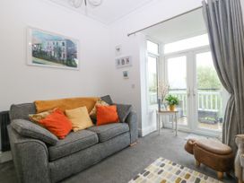 A living room with a grey sofa with pillows a small table with a plant and glass doors leading to a balcony at Terrace View in Trefriw near Llanrwst