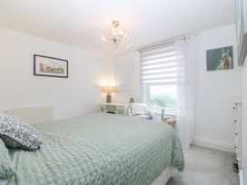 A bedroom with a green bedspread a chair a window with striped blinds and a chandelier at Terrace View in Trefriw near Llanrwst