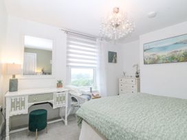 A bedroom with a bed green cover white dresser with a lamp and mirror wicker chair and window at Terrace View in Trefriw near Llanrwst