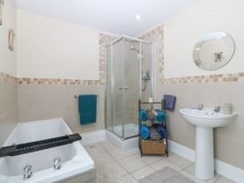 A bathroom with a bathtub shower cubicle sink towels and a round mirror at Terrace View in Trefriw near Llanrwst