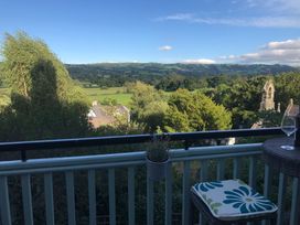 A balcony with a small table and cushion seating overlooking trees fields and distant hills at Terrace View in Trefriw near Llanrwst