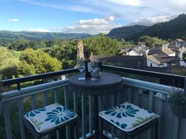 A balcony with a round table, two chairs with cushions and a bottle of wine with glasses overlooking hills and rooftops at Terrace View in Trefriw near Llanrwst