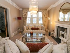 A living room with sofas pillows a glass coffee table a chandelier a floor lamp a fireplace and window curtains at Allendale House in Armathwaite