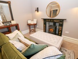 A sitting area with a green couch, multiple pillows, a beige ottoman, fireplace with a round mirror above it, a side table with photo frames and a wooden console table at Allendale House in Armathwaite