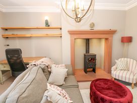 A living room with a wood burning stove a gray sofa a striped armchair and a red ottoman at Allendale House in Armathwaite