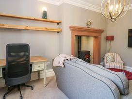 A living room with a desk chair, two wooden shelves, a fireplace with a stove, a sofa, an armchair, and a floor lamp at Allendale House in Armathwaite
