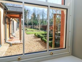 A view through a window showing a garden with gravel paths trimmed hedges small trees and wooden house structures at Allendale House in Armathwaite