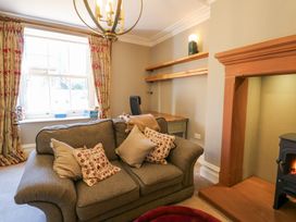A living room with a gray sofa and patterned cushions a wooden desk with floating shelves and a fireplace at Allendale House in Armathwaite