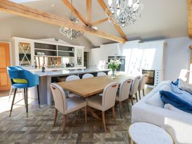 An open kitchen and dining area with a wooden dining table surrounded by beige chairs a sofa with blue cushions a kitchen island with a blue bar stool and pendant lights at Allendale House Armathwaite