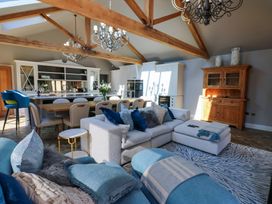 An open living space with a white sectional sofa and blue cushions a wooden dining table with chairs and a kitchen area with cabinets and a chandelier at Allendale House in Armathwaite