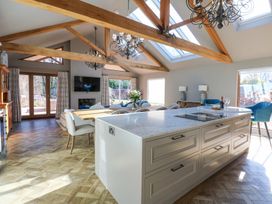 An open kitchen and dining area with a large island, dining table, chairs, chandeliers, wooden beams, skylights, and a television at Allendale House in Armathwaite
