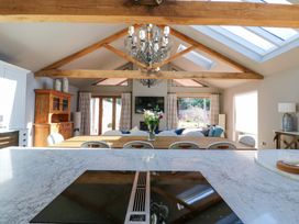 A kitchen island with a stove overlooking a dining table flowers and a living area with windows and wooden beams at Allendale House in Armathwaite