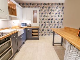 A kitchen with blue and white cabinets wooden countertops a microwave oven and patterned wallpaper at Allendale House in Armathwaite