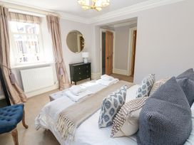 A bedroom with a bed covered with pillows and blankets a black dresser with a lamp a window with curtains and an open door at Allendale House in Armathwaite