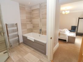 A bathroom with a bathtub, towel rack, and tiled walls next to a bedroom with a bed, chair, and chandelier at Allendale House in Armathwaite