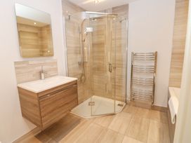 A bathroom with a corner glass shower enclosure a wooden vanity with sink a wall mirror heated towel rail and a bathtub at Allendale House in Armathwaite