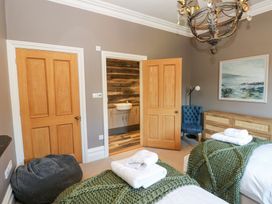 A bedroom with two beds covered with green knitted blankets and white towels a wooden dresser a blue chair a door open to a bathroom with a sink and wood-patterned tiles at Allendale House in Armathwaite