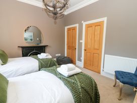 A bedroom with two single beds with green throws and white towels a fireplace with a round mirror above two wooden doors and a blue chair at Allendale House Armathwaite