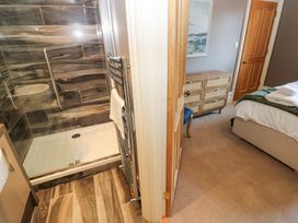 A bathroom with a glass shower and wooden tile floor next to a bedroom with a bed and dresser at Allendale House in Armathwaite