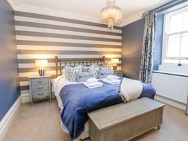 A bedroom with a double bed blue bedding two bedside tables with lamps a chest at the foot of the bed and a window with patterned curtains at Allendale House in Armathwaite