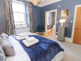 A bedroom with a bed folded towels on a blue blanket a window with curtains a chair a chest of drawers with a lamp and an open door leading to a bathroom at Allendale House in Armathwaite