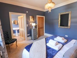 A bedroom with a bed with folded towels on top a chair a dresser with a lamp and an open door leading to a bathroom at Allendale House in Armathwaite