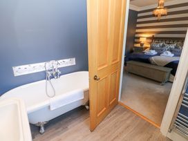 A bathroom with a clawfoot bathtub and a wooden door leading to a bedroom with a bed and striped wallpaper at Allendale House in Armathwaite