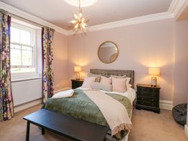 A bedroom with a double bed two bedside tables table lamps floral curtains and a round mirror above the bed at Allendale House in Armathwaite