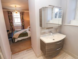 A bedroom with a bed and floral curtains next to a bathroom sink with a mirror cabinet at Allendale House in Armathwaite