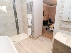 A bathroom with a walk-in shower towel rack and sink with a glass and an adjacent bedroom with a chair and bedside table at Allendale House in Armathwaite