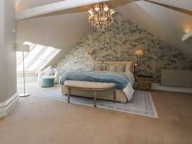 A bedroom with a bed a bench a nightstand a floor lamp an armchair and a chandelier at Allendale House in Armathwaite