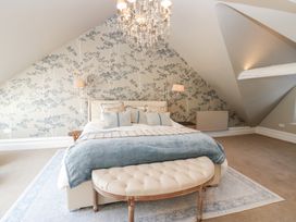 A bedroom with a bed a cushioned bench a chandelier and floral wallpaper at Allendale House in Armathwaite