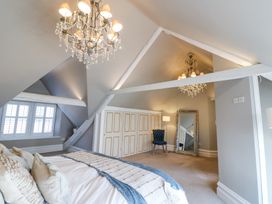 A bedroom with a chandelier bed pillows blue chair and large mirror at Allendale House in Armathwaite