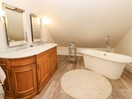 A bathroom with a wooden vanity and two mirrors a freestanding bathtub and a small round table at Allendale House in Armathwaite
