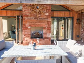An outdoor seating area with a white wicker table and cushioned chairs a bottle and glasses on the table a stone fireplace and wood panel doors at Allendale House in Armathwaite