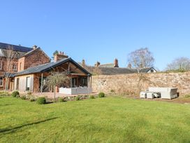 A garden with a wooden patio, outdoor seating, and a stone wall at Allendale House in Armathwaite
