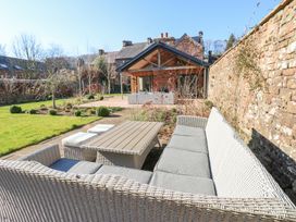 An outdoor seating area with wicker furniture and cushions next to a stone wall and garden at Allendale House in Armathwaite