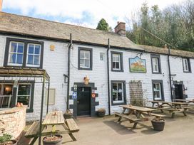 An outdoor seating area with wooden picnic tables in front of a white stone building with black window frames at Allendale House in Armathwaite