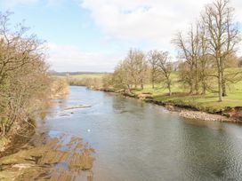 A river flowing with trees on both sides and grassy fields at Allendale House in Armathwaite