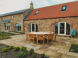 A stone patio with a round wooden table and chairs outside a stone building with red roof tiles at The Old Watermill in Beadnell